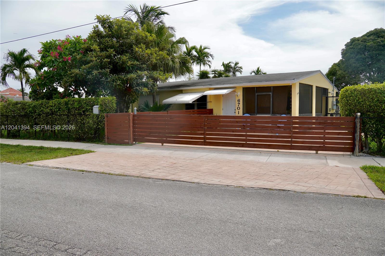 A yellow house with a screened porch is enclosed by a horizontal wood slat fence — 6701 Harding St, Hollywood FL 33024, HOLLYWOOD, FL