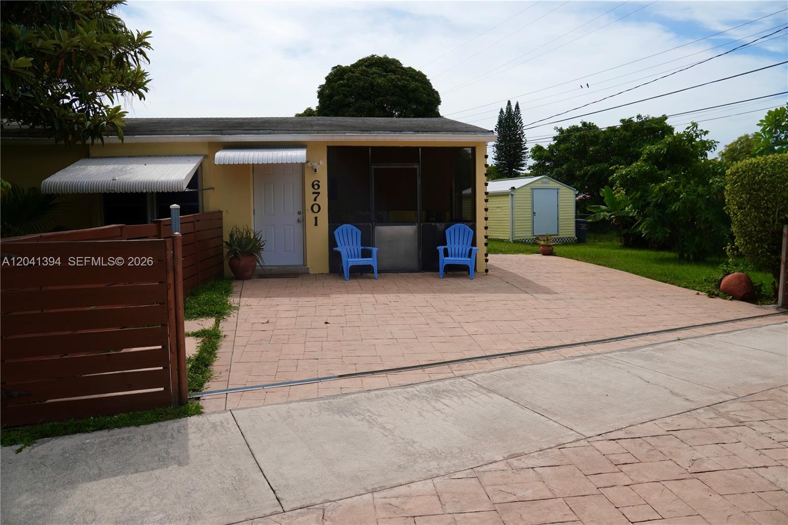 A yellow house features a screened porch, a paved driveway, and two blue chairs — 6701 Harding St, Hollywood FL 33024, HOLLYWOOD, FL