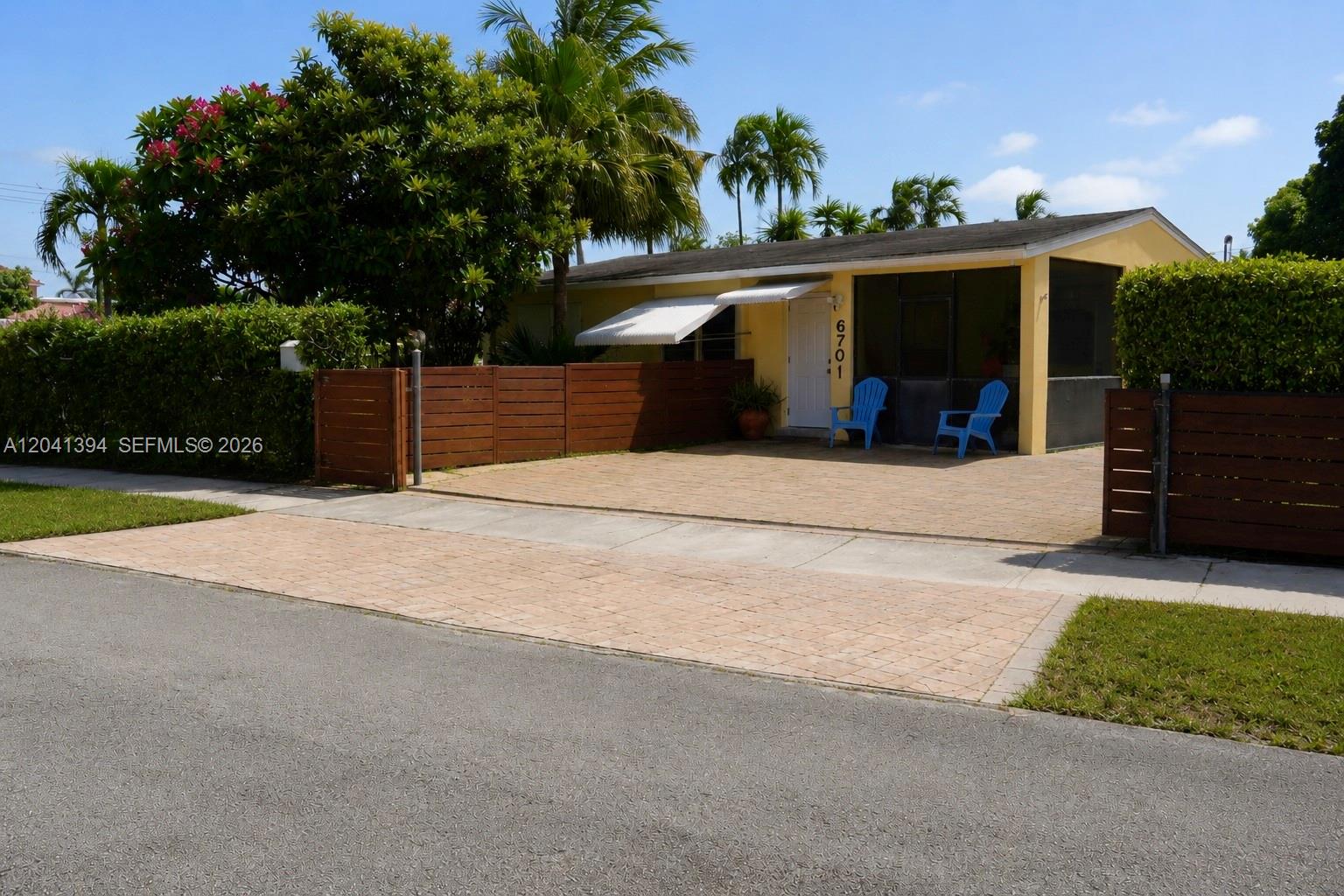 A yellow single-story house features a paved driveway, a wooden fence, and a screened porch — 6701 Harding St, Hollywood FL 33024, HOLLYWOOD, FL