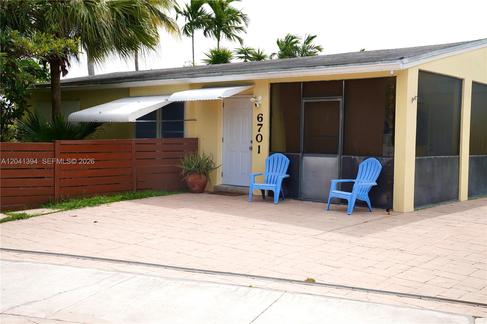 A yellow house features a paved front patio, two blue chairs, and a screened porch — 6701 Harding St, Hollywood FL 33024, HOLLYWOOD, FL