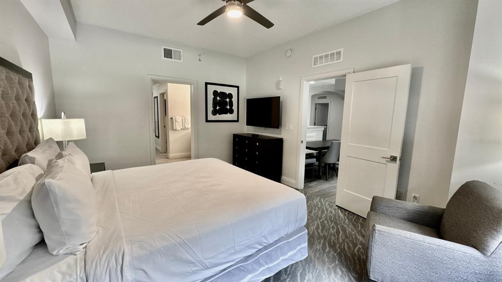 A bedroom features a king bed, a dark dresser with a television, and an armchair — 14501 GROVE RESORT AVENUE UNIT 3202, WINTER GARDEN, FL