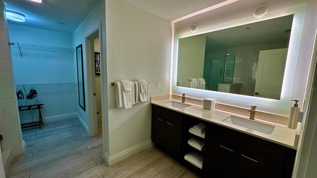 A bathroom features a double vanity with a backlit mirror and an adjacent walk-in closet — 14501 GROVE RESORT AVENUE UNIT 3202, WINTER GARDEN, FL