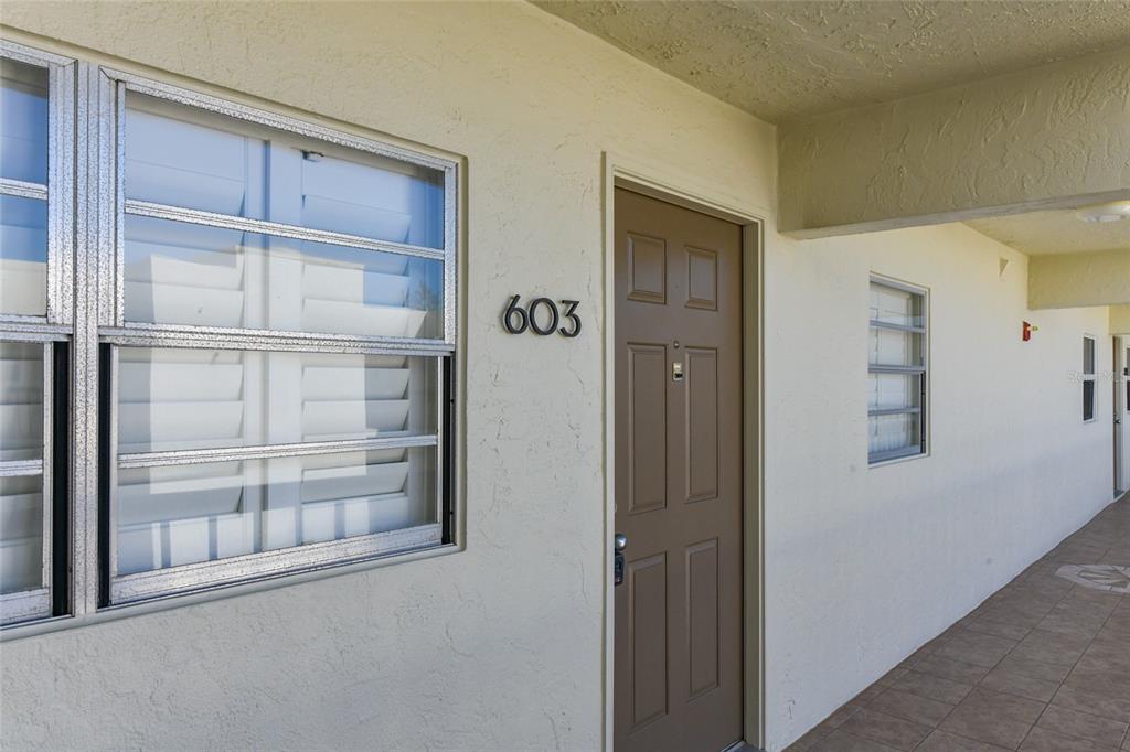 A brown front door labeled 603 is set into a beige exterior wall with jalousie windows — 3240 GULF OF MEXICO DRIVE UNIT 603, LONGBOAT KEY, FL