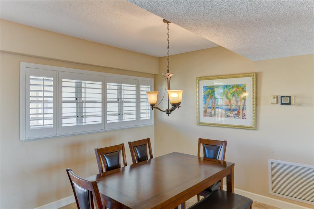 A dining room features a wooden table, dark chairs, a chandelier, and plantation shutters — 3240 GULF OF MEXICO DRIVE UNIT 603, LONGBOAT KEY, FL