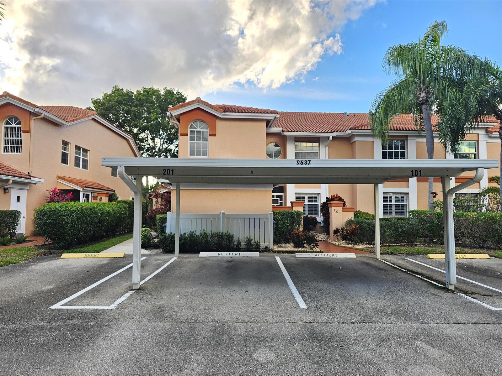 A covered parking structure with two resident spaces sits in front of a multi-story building — 9637 Shadybrook Drive # 201, Boynton Beach FL 33437, BOYNTON BEACH, FL