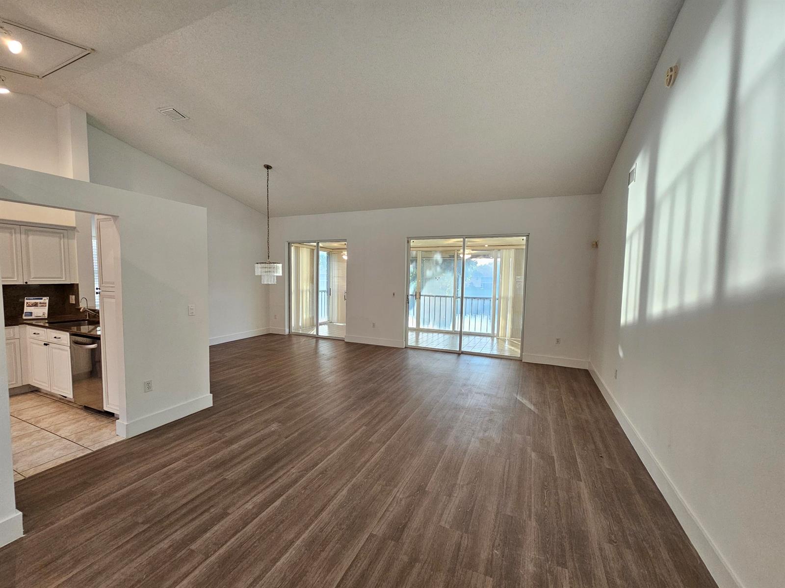 An open-concept living area features wood-look flooring, white walls, and sliding glass doors to a balcony — 9637 Shadybrook Drive # 201, Boynton Beach FL 33437, BOYNTON BEACH, FL