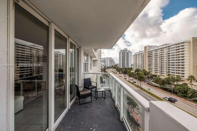 A balcony with dark flooring, outdoor furniture, and a glass railing overlooking a city street — 5601 Collins Ave # 825, Miami Beach FL 33140, MIAMI BEACH, FL
