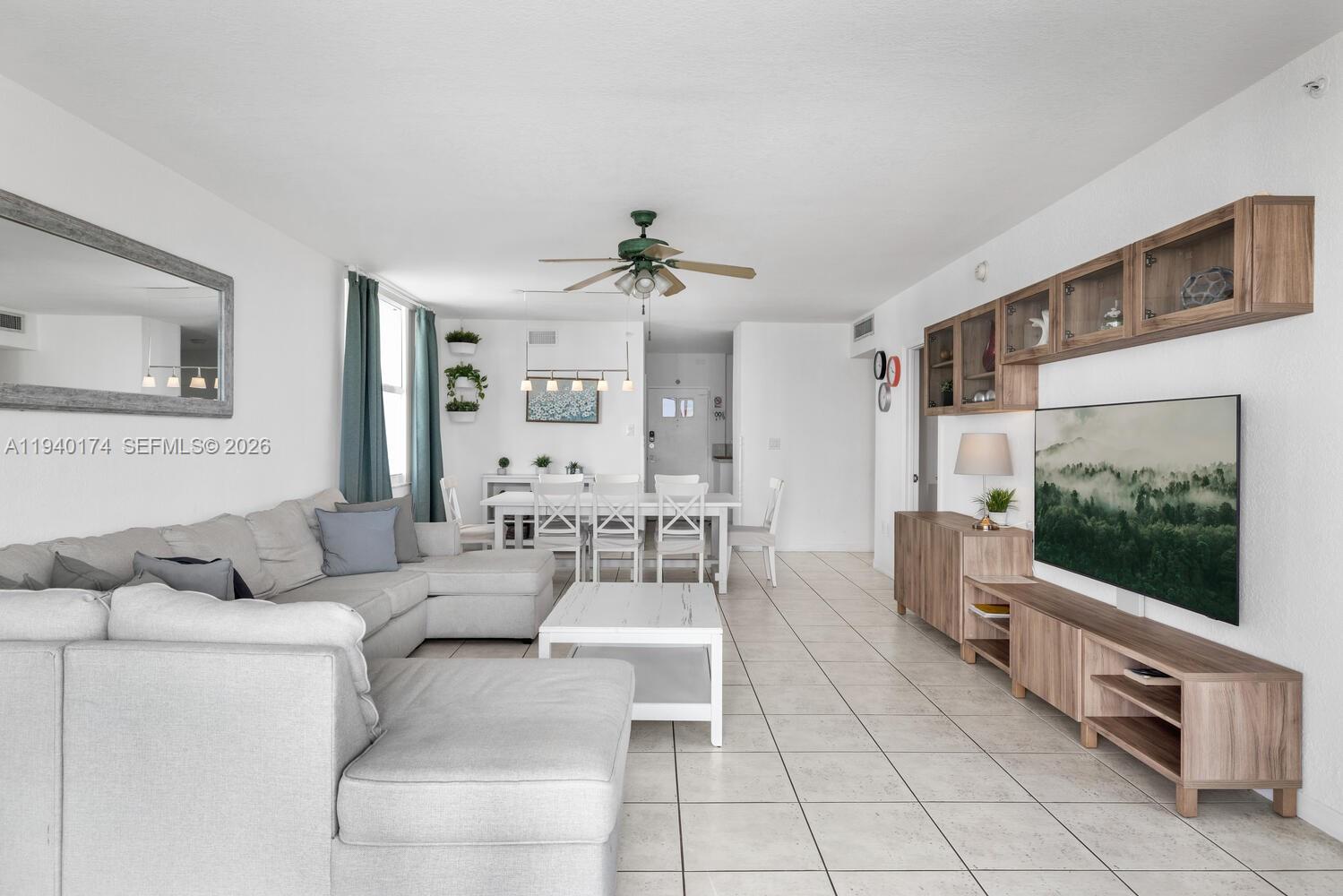 A living and dining area features white tile floors, a sectional sofa, and wood cabinetry — 5601 Collins Ave # 825, Miami Beach FL 33140, MIAMI BEACH, FL