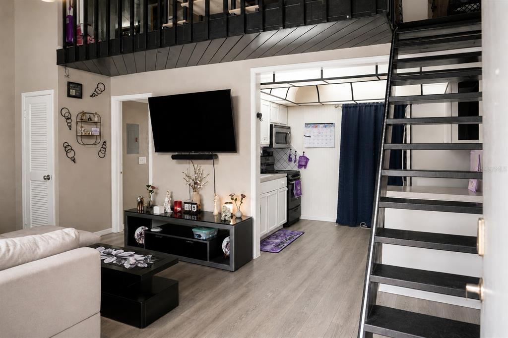 A living room with a television, media console, and stairs leading to a loft area — 2142 BRADFORD STREET UNIT 308, CLEARWATER, FL