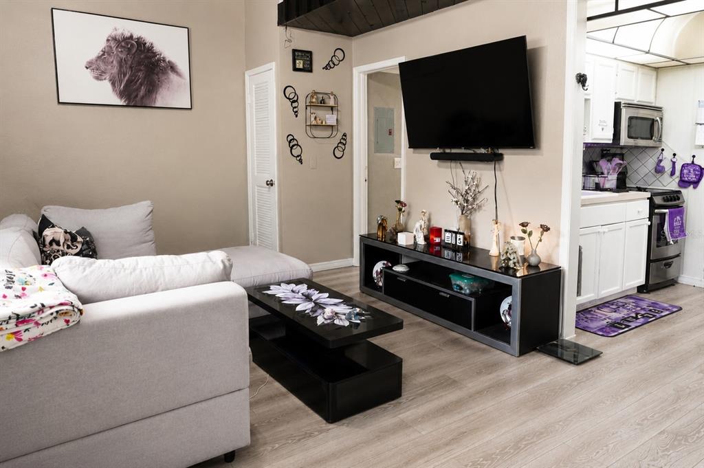 A living room features light wood flooring, a grey sectional sofa, and a black media console — 2142 BRADFORD STREET UNIT 308, CLEARWATER, FL