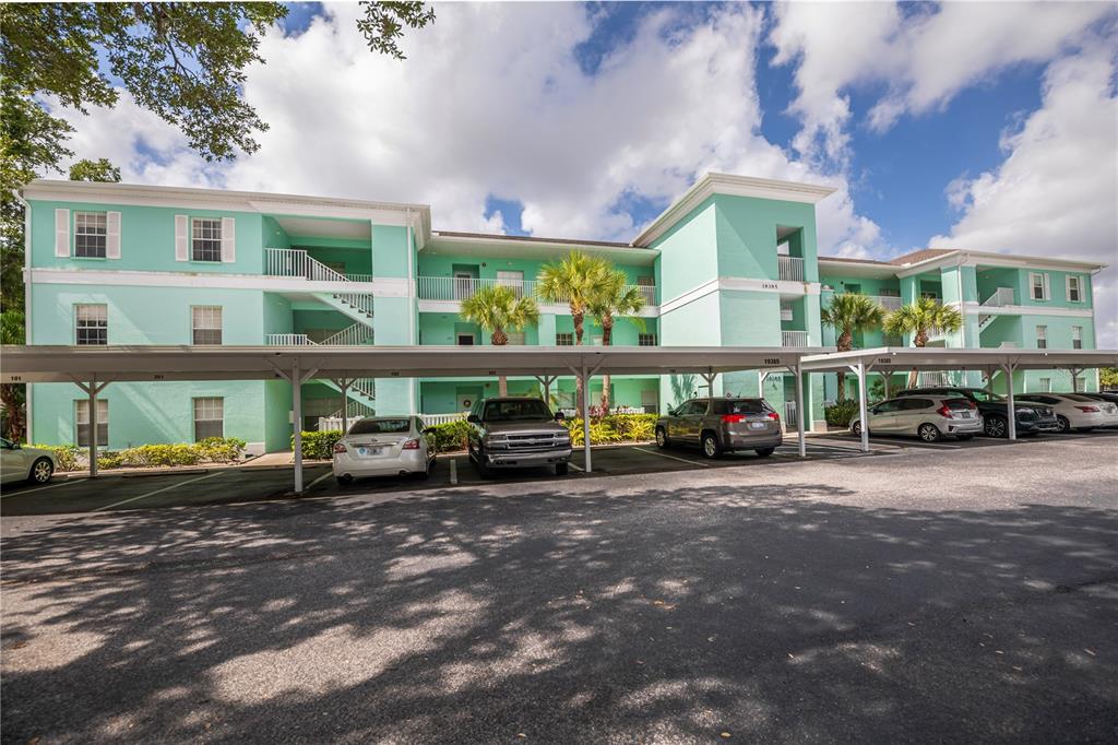 A three-story, light green apartment building features covered parking spaces in the foreground — 19385 WATER OAK DRIVE UNIT 301, PORT CHARLOTTE, FL