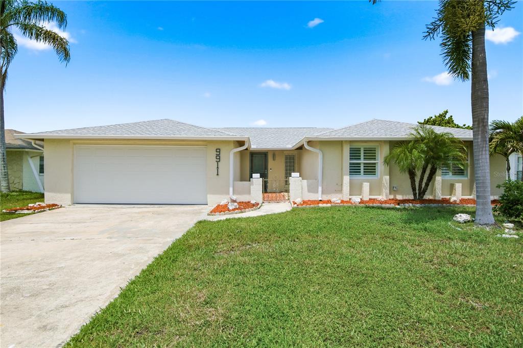 A single-story house with a white garage, beige stucco exterior, and a small front courtyard — 9911 ISLAND HARBOR DRIVE, PORT RICHEY, FL