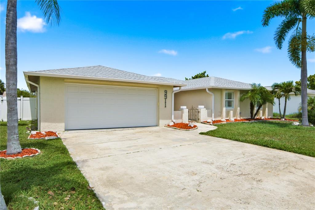 A single-story house with a white garage door, beige stucco walls, and a concrete driveway — 9911 ISLAND HARBOR DRIVE, PORT RICHEY, FL