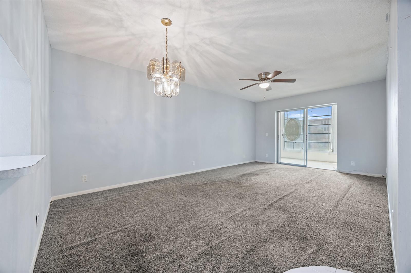 An empty living room with gray carpet, light blue walls, a chandelier, and sliding glass doors — 230 NE 26th Avenue # 206, Boynton Beach FL 33435, BOYNTON BEACH, FL