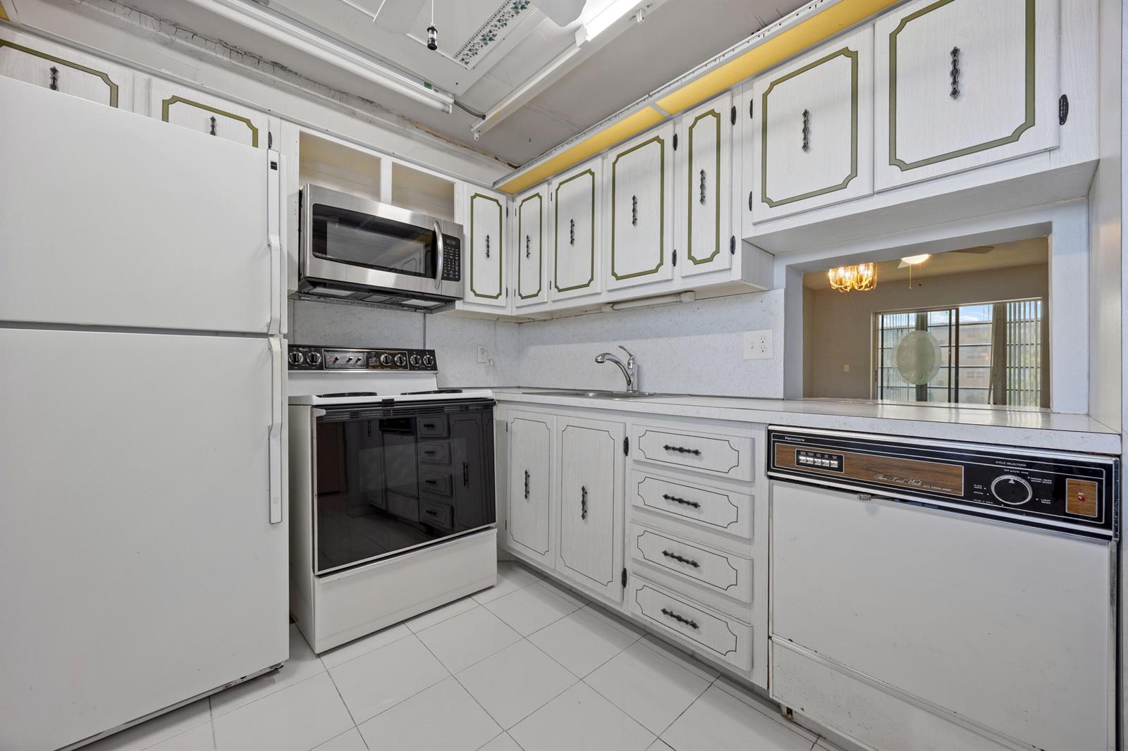 A kitchen features white cabinetry with green trim, white appliances, and a pass-through window — 230 NE 26th Avenue # 206, Boynton Beach FL 33435, BOYNTON BEACH, FL