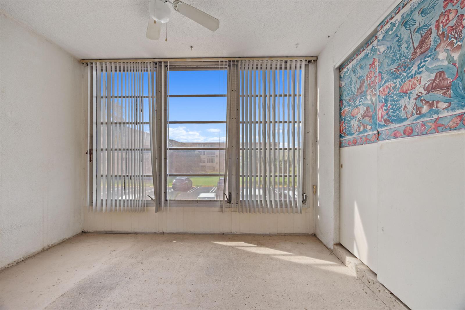 An empty room features a large window with vertical blinds, a ceiling fan, and wallpaper — 230 NE 26th Avenue # 206, Boynton Beach FL 33435, BOYNTON BEACH, FL
