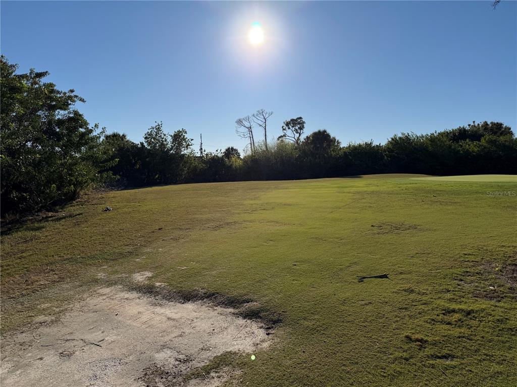 A grassy, sunlit lot features a sandy patch in the foreground and surrounding trees — 2 PINE VALLEY PL, ROTONDA WEST, FL