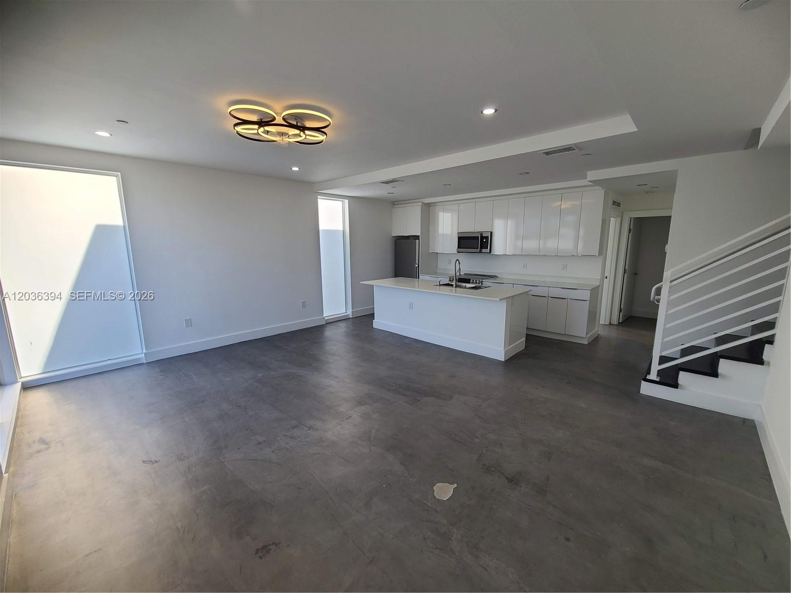 An open-concept kitchen and living area features white cabinetry, a central island, and concrete floors — 825 Michigan Ave # 7, Miami Beach FL 33139, MIAMI BEACH, FL