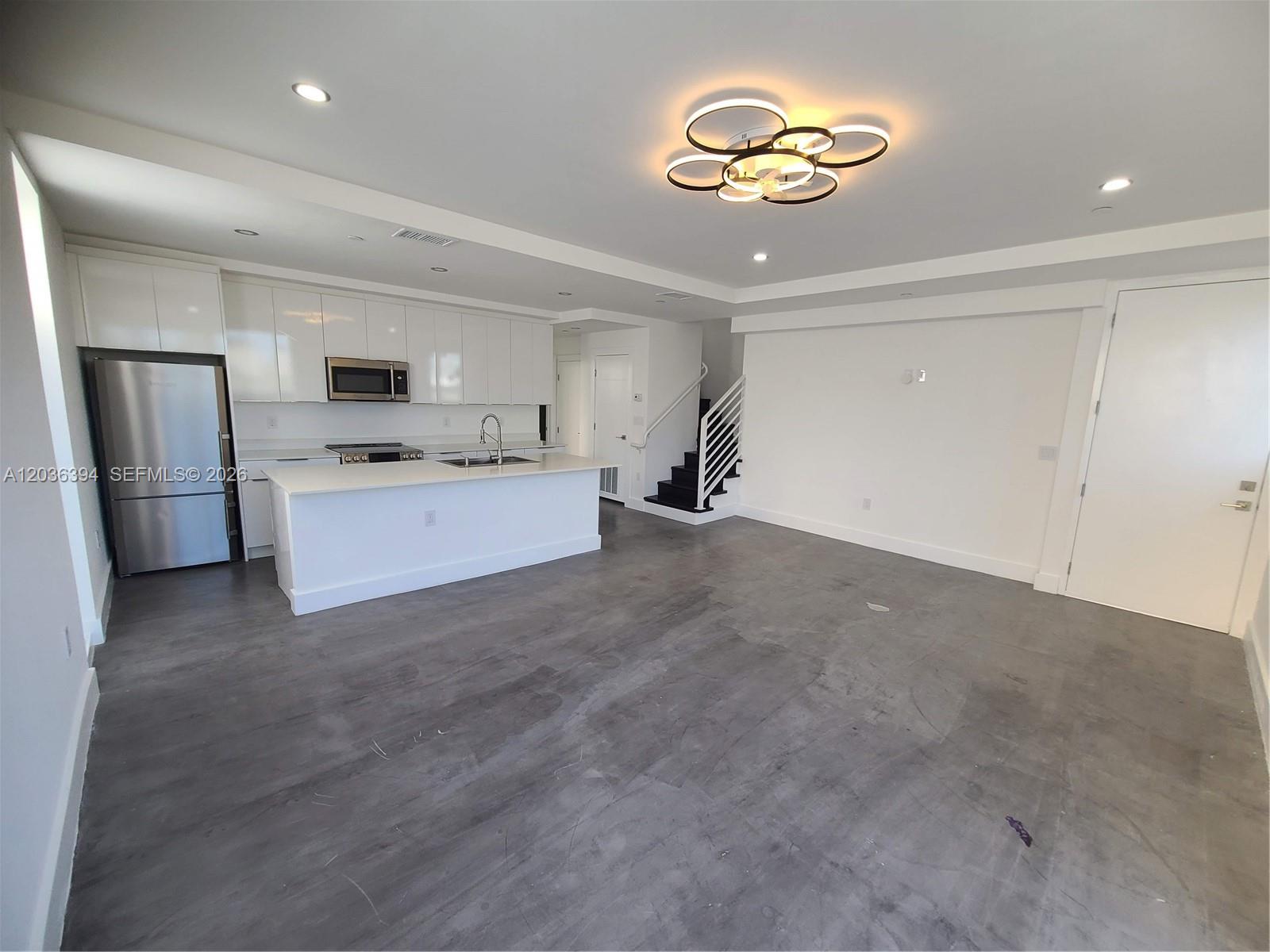 A modern kitchen with white cabinetry and an island opens into a spacious living area — 825 Michigan Ave # 7, Miami Beach FL 33139, MIAMI BEACH, FL