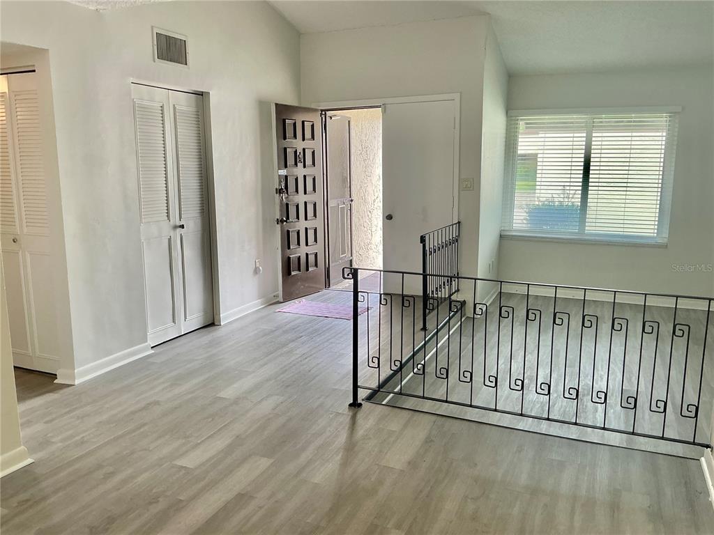 An entryway with light wood-look flooring, a metal stair railing, and a white front door — 2207 BELLEAIR ROAD UNIT B22, CLEARWATER, FL