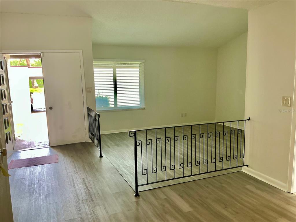 An entryway with light wood-look flooring leads to a sunken living area with metal railings — 2207 BELLEAIR ROAD UNIT B22, CLEARWATER, FL