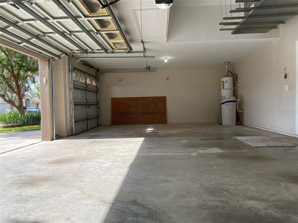 An empty two-car garage with a concrete floor, water heater, and open garage door — 10542 SAN TRAVASO DRIVE, TAMPA, FL