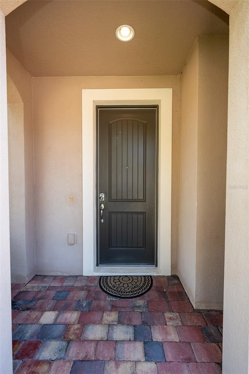 A dark front door with a welcome mat sits in a covered entryway with pavers — 12077 ULETA LANE, ORLANDO, FL