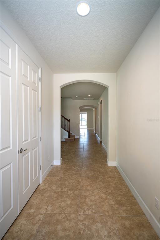 A tiled hallway leads through arched doorways toward a staircase and a distant window — 12077 ULETA LANE, ORLANDO, FL