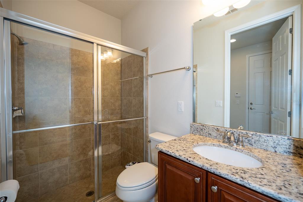 A bathroom features a glass-enclosed shower, a toilet, and a granite-topped vanity with wood cabinets — 12077 ULETA LANE, ORLANDO, FL