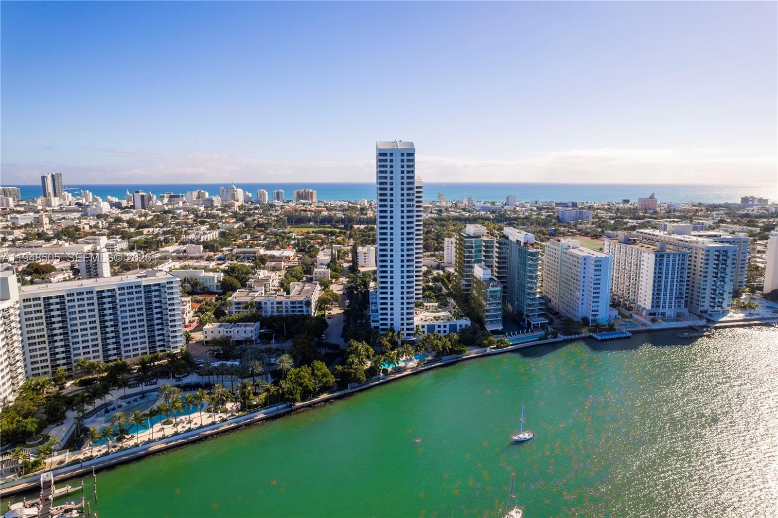 An aerial view shows a tall residential tower surrounded by buildings near a coastal waterway — 1330 West Ave # 610, Miami Beach FL 33139, MIAMI BEACH, FL