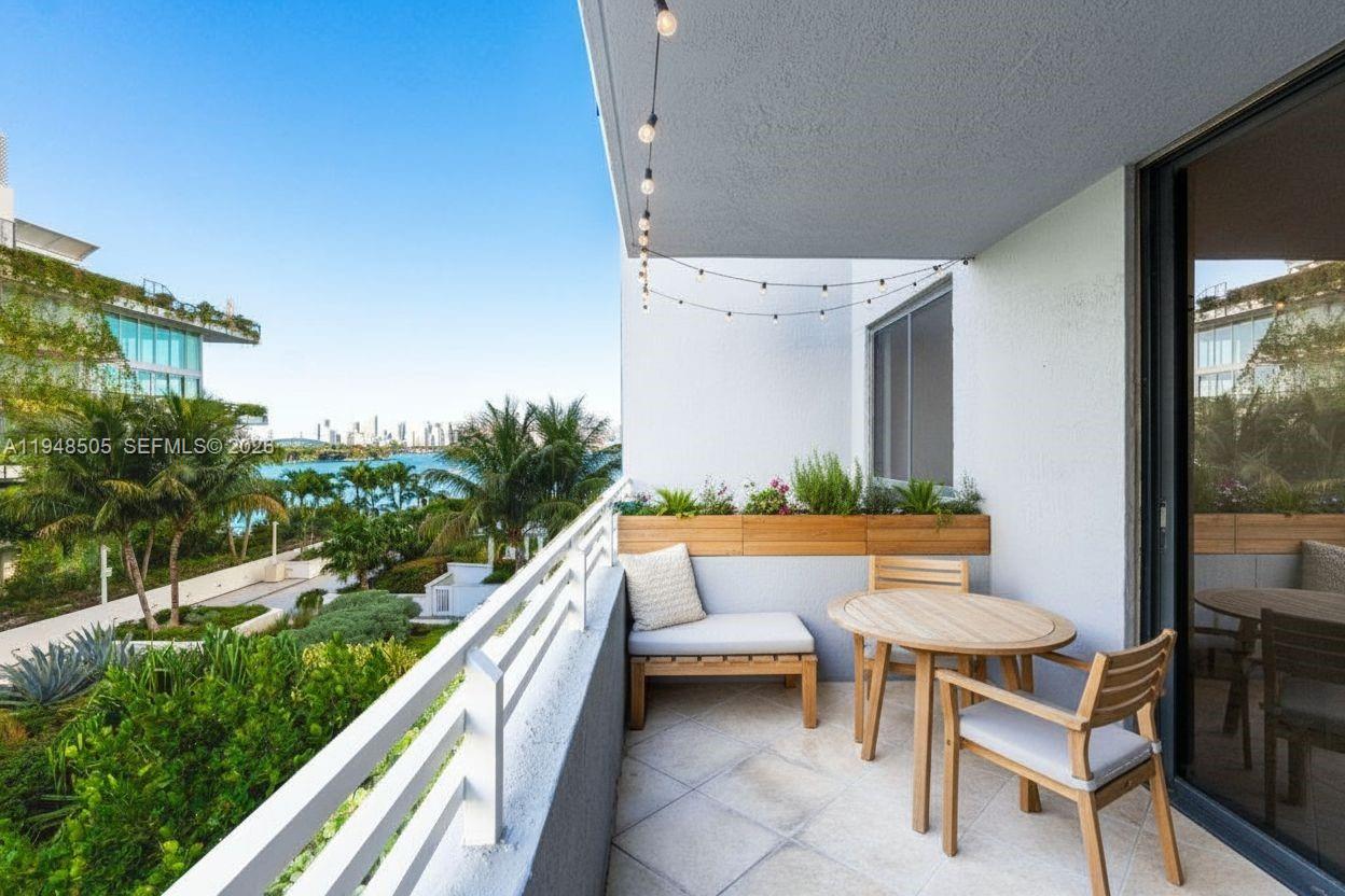 A balcony features a wooden table, chairs, a bench, and string lights overlooking a waterfront — 1330 West Ave # 610, Miami Beach FL 33139, MIAMI BEACH, FL