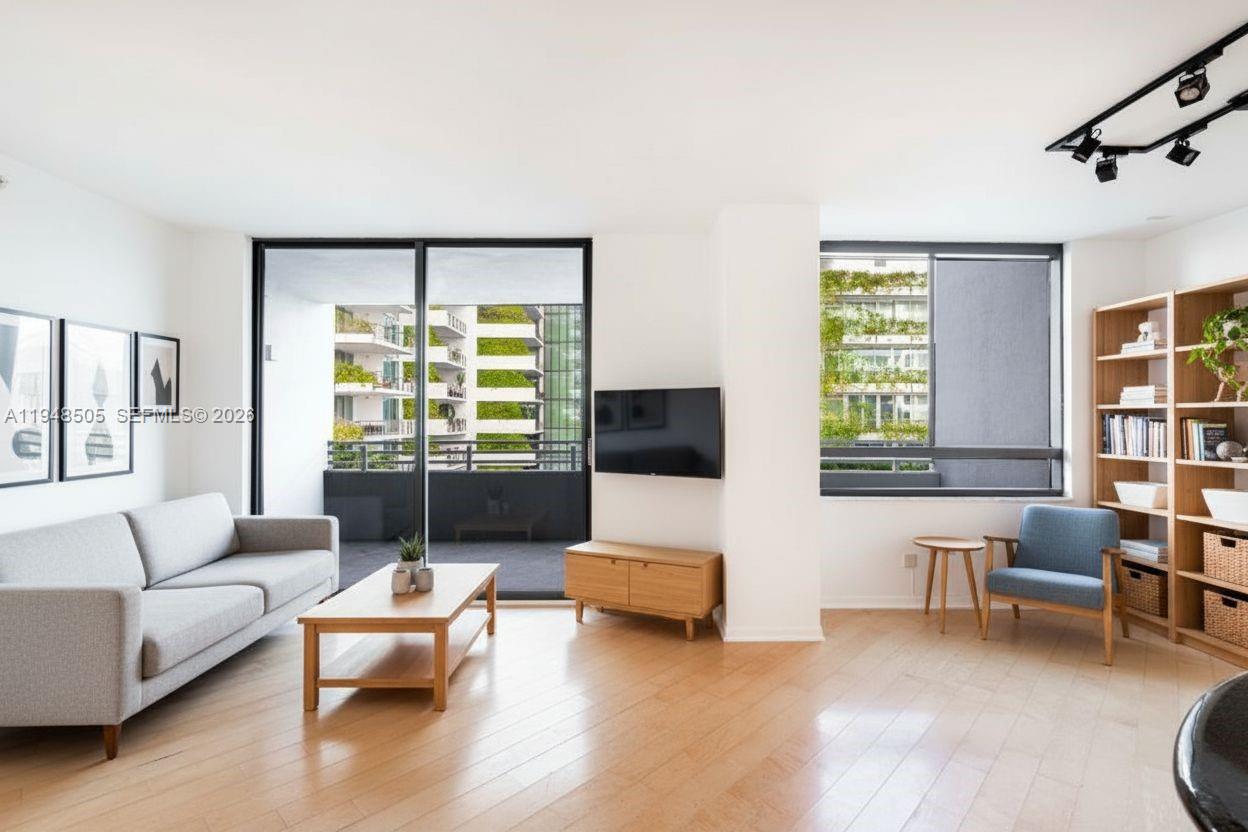 A living room features light wood floors, a grey sofa, a television, and a balcony — 1330 West Ave # 610, Miami Beach FL 33139, MIAMI BEACH, FL