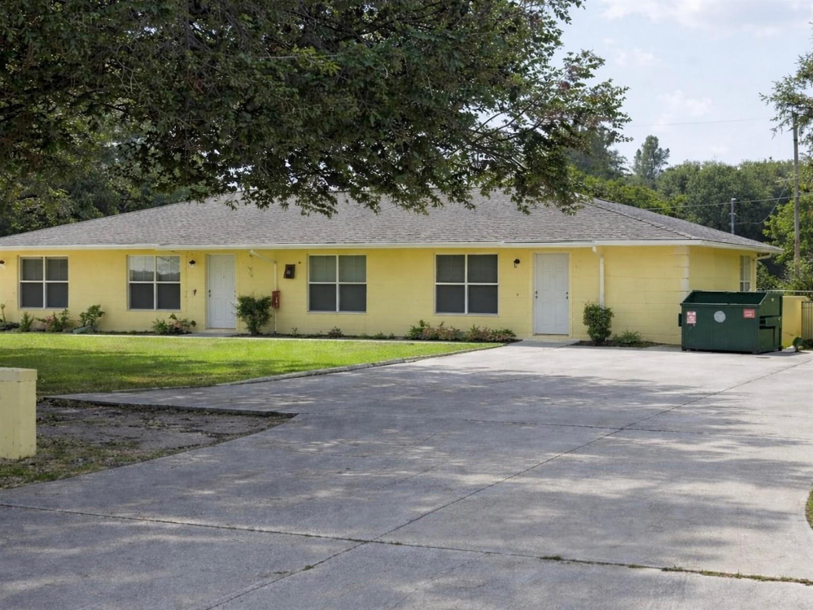 A yellow single-story duplex with a large concrete driveway and a green dumpster — 951 King Orange Drive, Fort Pierce FL 34982, FORT PIERCE, FL