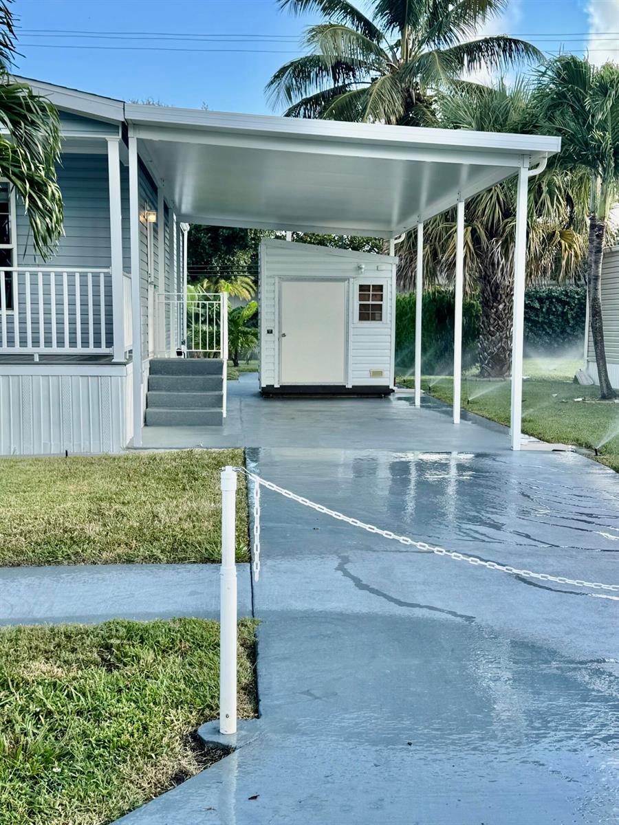 A carport with a white shed sits beside a house with gray steps and siding — 133 NW 53 Place, Deerfield Beach FL 33064, DEERFIELD BEACH, FL