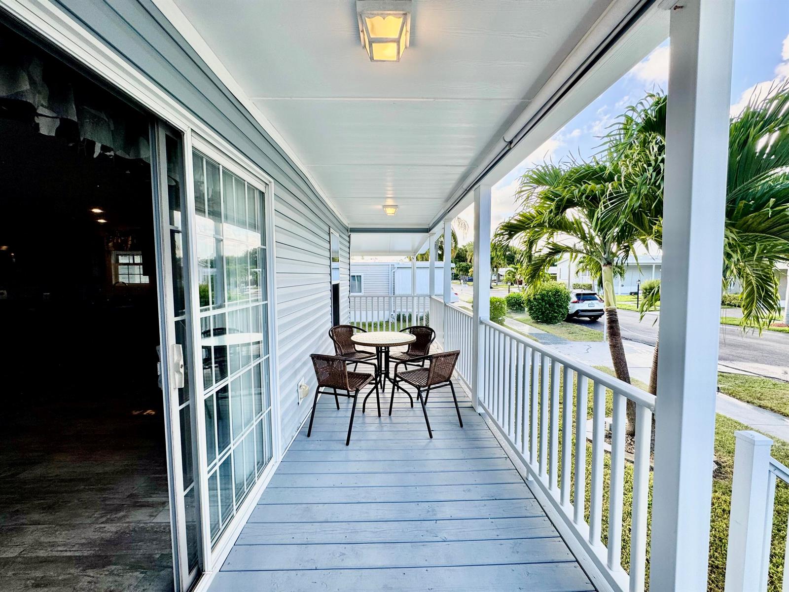 A covered porch features light blue wooden decking, white railings, and a small bistro set — 133 NW 53 Place, Deerfield Beach FL 33064, DEERFIELD BEACH, FL