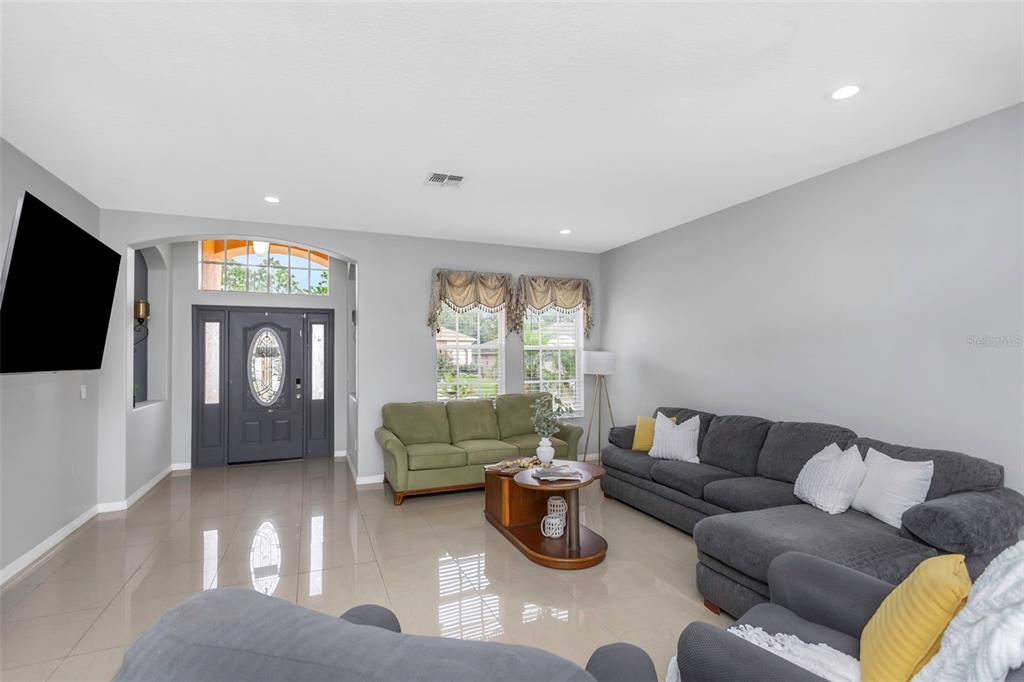 A living room features light tile flooring, gray walls, a sectional sofa, and a green sofa — 14818 EDGEMERE DRIVE, SPRING HILL, FL