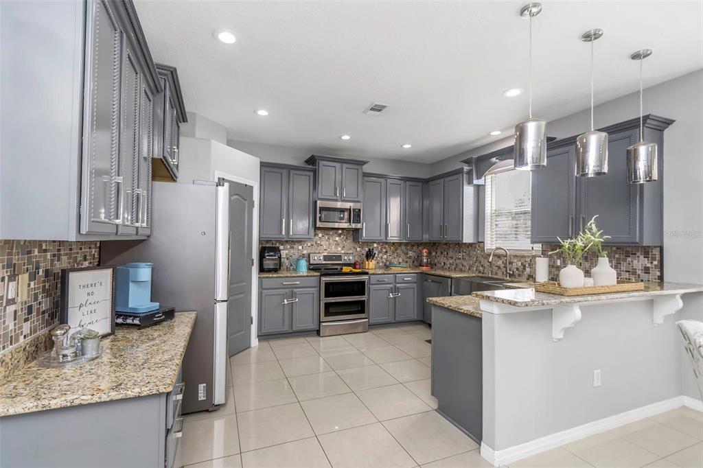 A kitchen features gray cabinets, granite countertops, stainless steel appliances, and a tiled floor — 14818 EDGEMERE DRIVE, SPRING HILL, FL