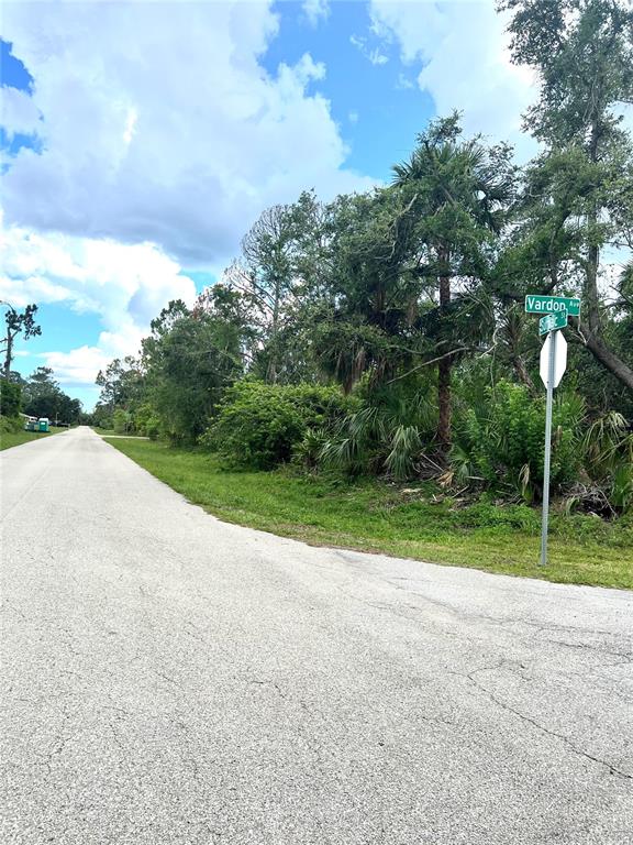 A paved road leads to a corner lot with dense trees and a street sign — 18235 VARDON AVENUE, PORT CHARLOTTE, FL