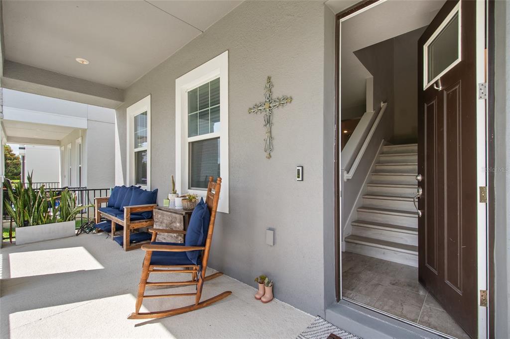 A covered front porch features a wooden rocking chair, a bench, and an open front door — 2241 WHITE FEATHER LOOP, WINTER GARDEN, FL