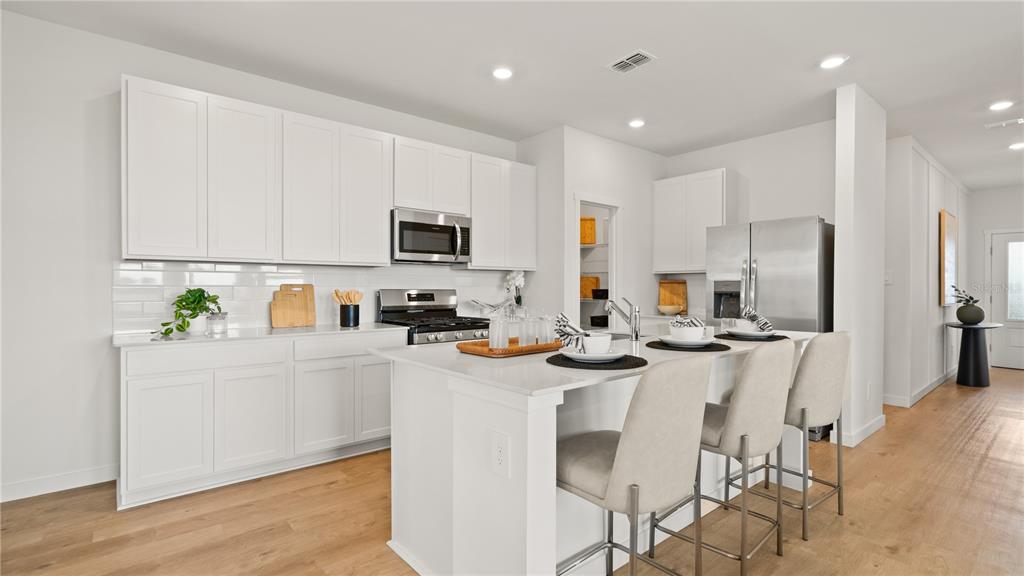 A modern kitchen features white cabinetry, stainless steel appliances, a center island, and light wood flooring — 4161 EASTMINSTER ROAD, DAVENPORT, FL