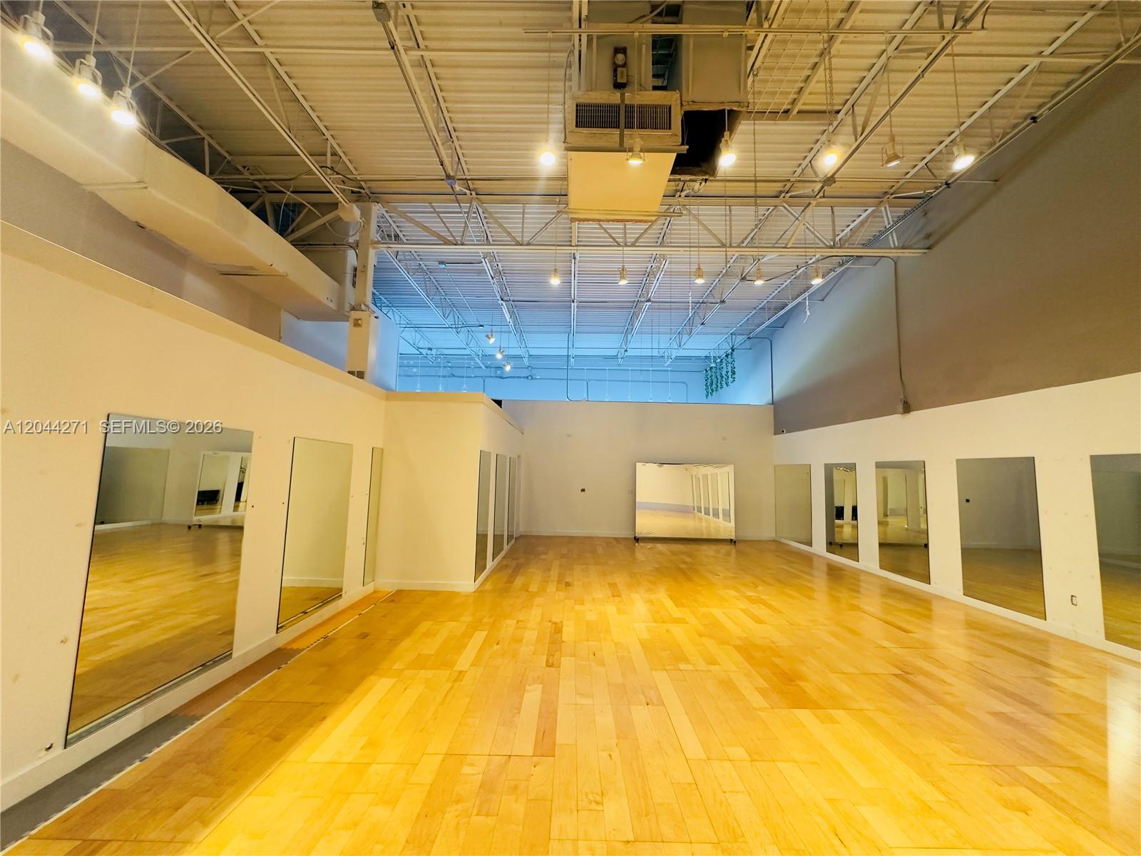 This studio space features light wood flooring, mirrored walls, and an exposed industrial ceiling — Confidential, North Miami Beach FL 33160, NORTH MIAMI BEACH, FL