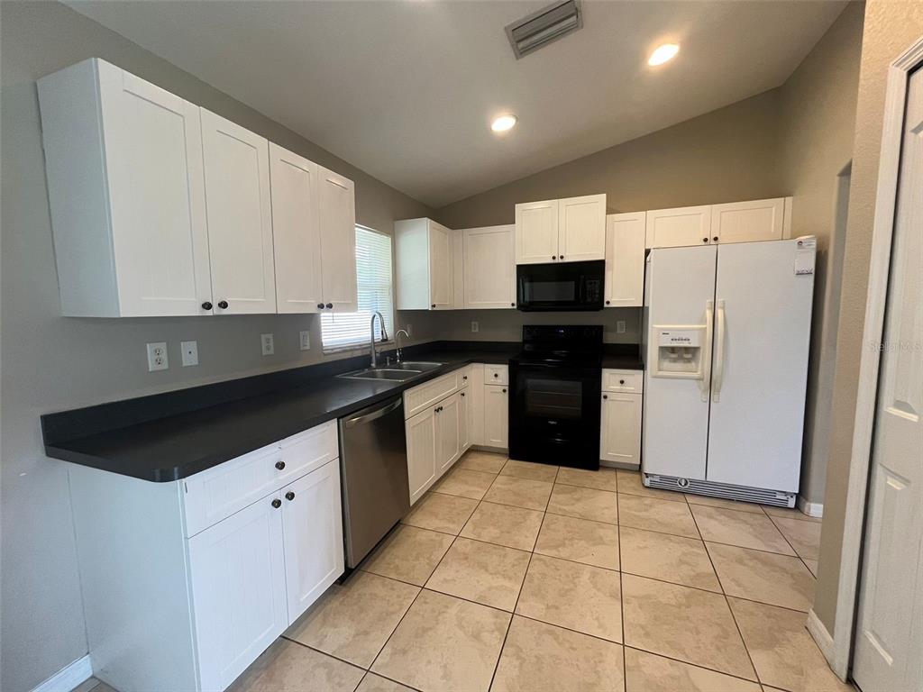 A kitchen features white cabinets, black countertops, stainless steel appliances, and beige tile flooring — 3605 CABALLERO AVENUE, NORTH PORT, FL