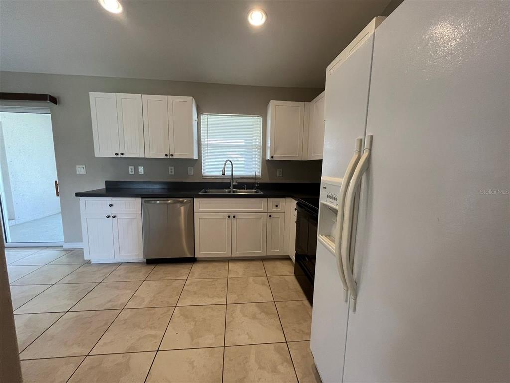 A kitchen features white cabinets, dark countertops, stainless steel appliances, and light-colored tile flooring — 3605 CABALLERO AVENUE, NORTH PORT, FL