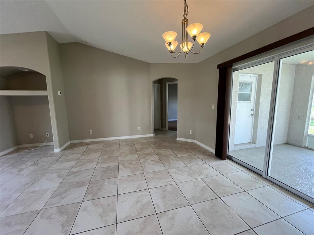 A living room with beige tile flooring, a vaulted ceiling, and a sliding glass door — 3605 CABALLERO AVENUE, NORTH PORT, FL