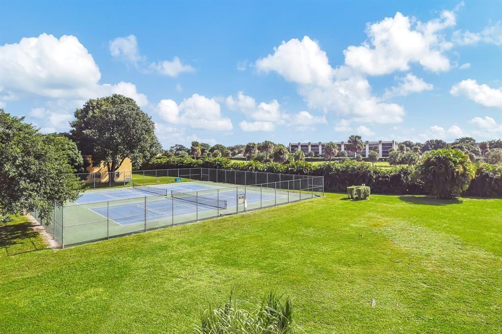 An outdoor tennis court sits next to a large grassy lawn under a blue sky — 9300 SW 8th Street # 422, Boca Raton FL 33428, BOCA RATON, FL
