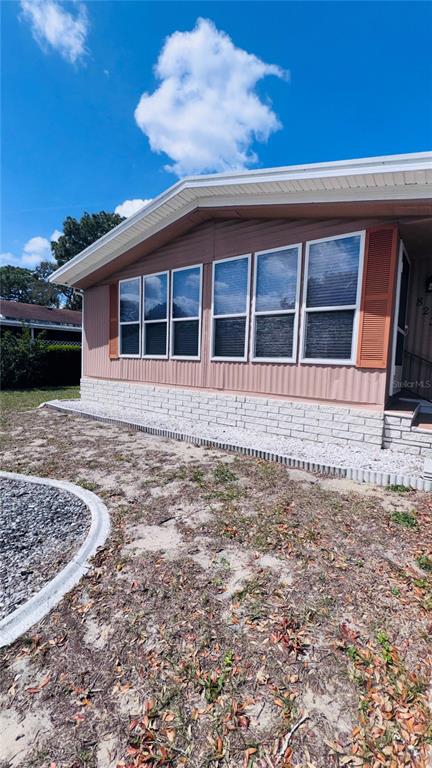 The exterior of a mobile home features tan siding, a brick-patterned base, and multiple windows — 8239 RIDGE DALE AVENUE, BROOKSVILLE, FL