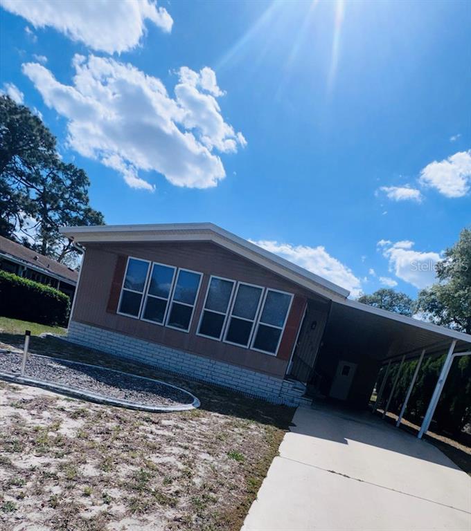 A single-story manufactured home features a tan exterior, a carport, and a gravel landscaping bed — 8239 RIDGE DALE AVENUE, BROOKSVILLE, FL