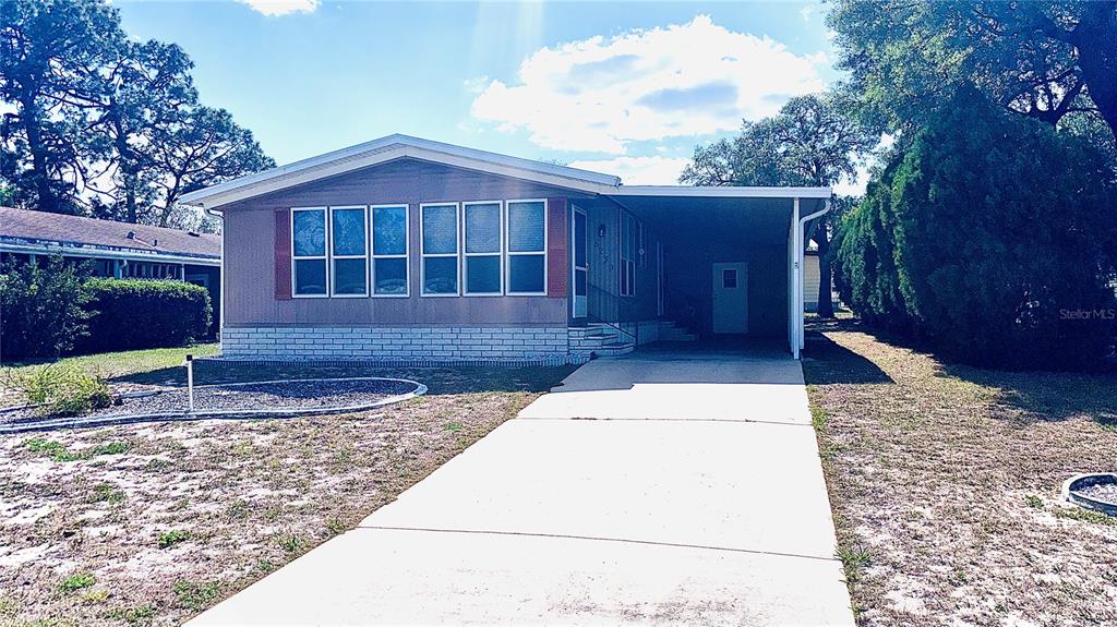 A single-story manufactured home features a tan exterior, a concrete driveway, and a covered carport — 8239 RIDGE DALE AVENUE, BROOKSVILLE, FL