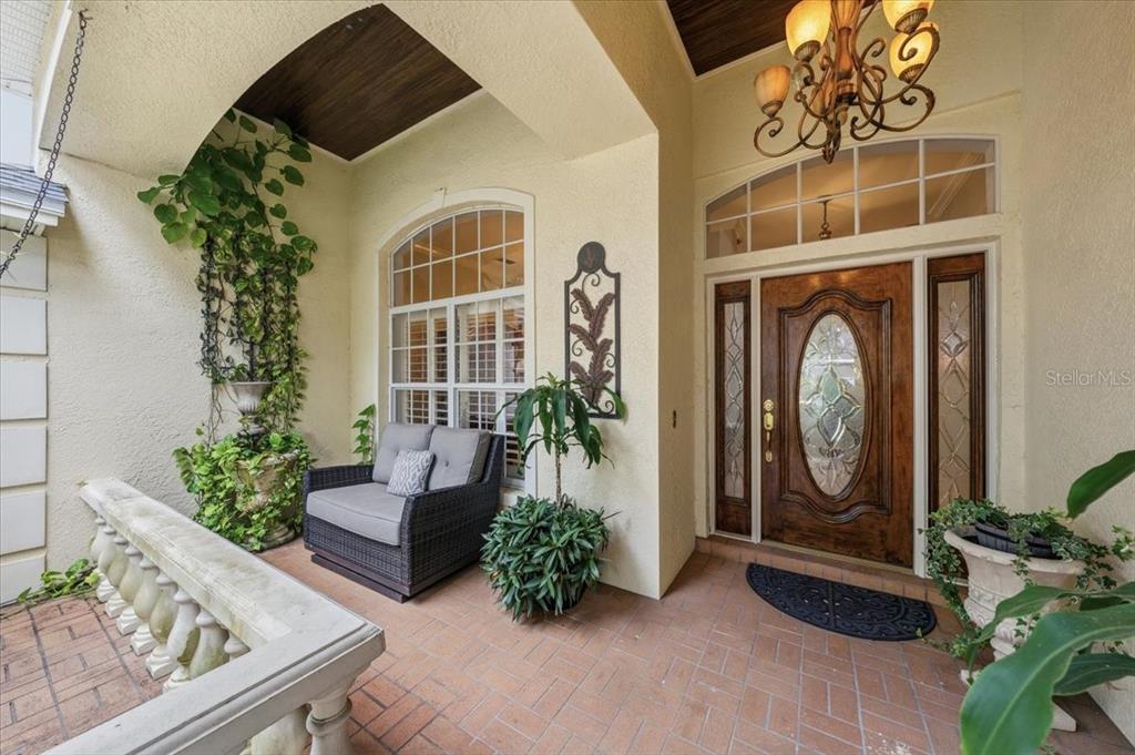 A covered entryway features a wooden front door, a chandelier, and a small seating area — 4941 FELECITY WAY, PALM HARBOR, FL