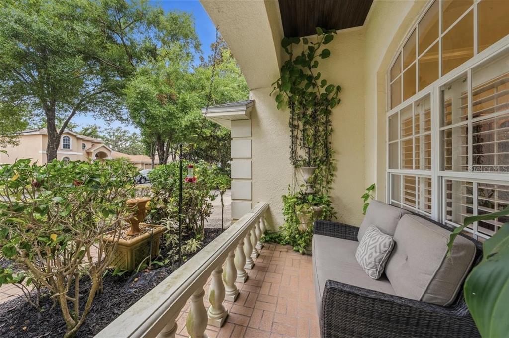 A covered porch features a wicker sofa, a stone fountain, and climbing vines on the wall — 4941 FELECITY WAY, PALM HARBOR, FL
